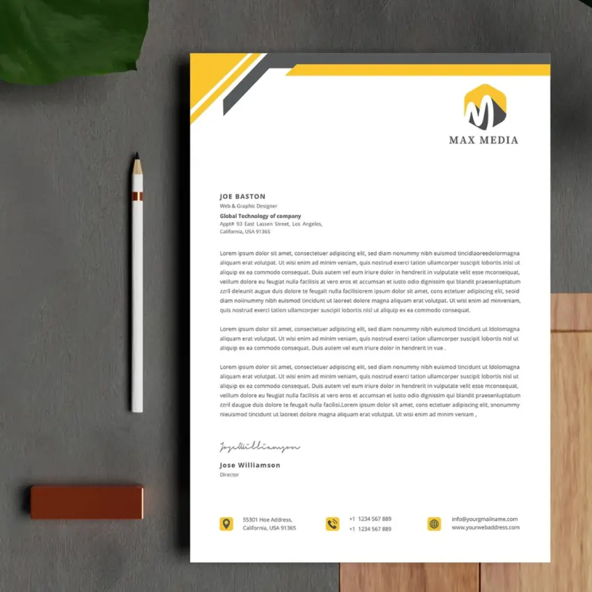 A close-up of a custom letterhead with a yellow and black design on a gray surface, with a pencil and a plant nearby.
