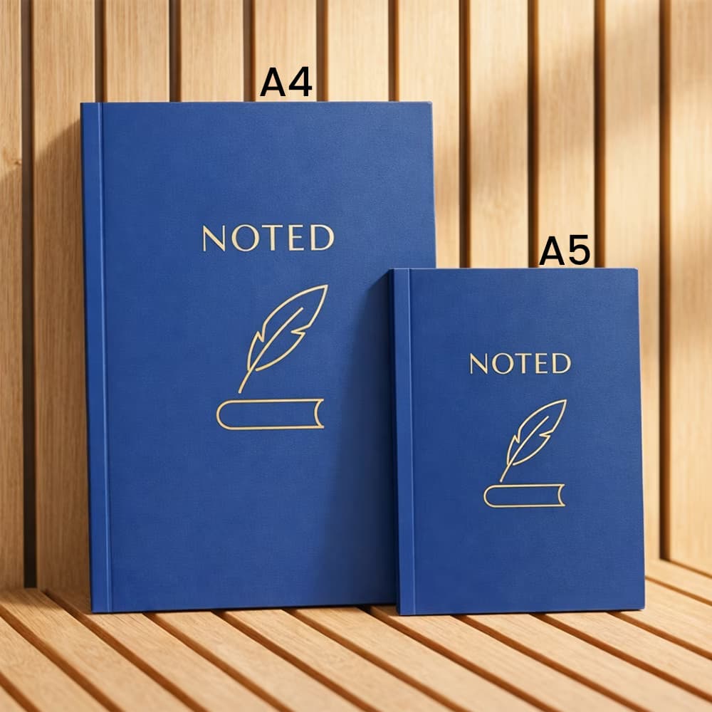 A side-by-side size comparison of two classic blue softbound notebooks labeled A4 and A5, with gold feather logos, on a wood background.