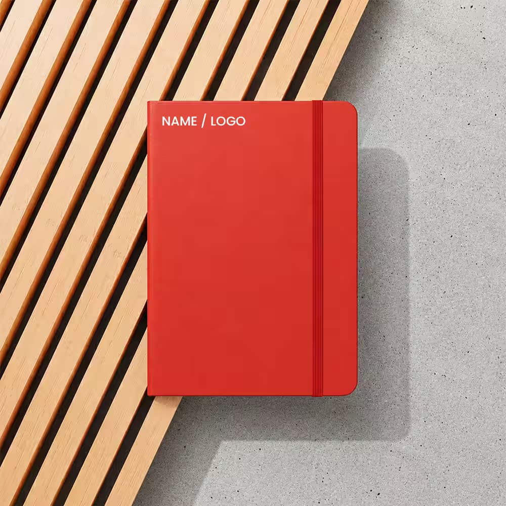 Top-down view of a red personalized diary with an elastic band, placed on a wooden slatted surface and concrete ground.