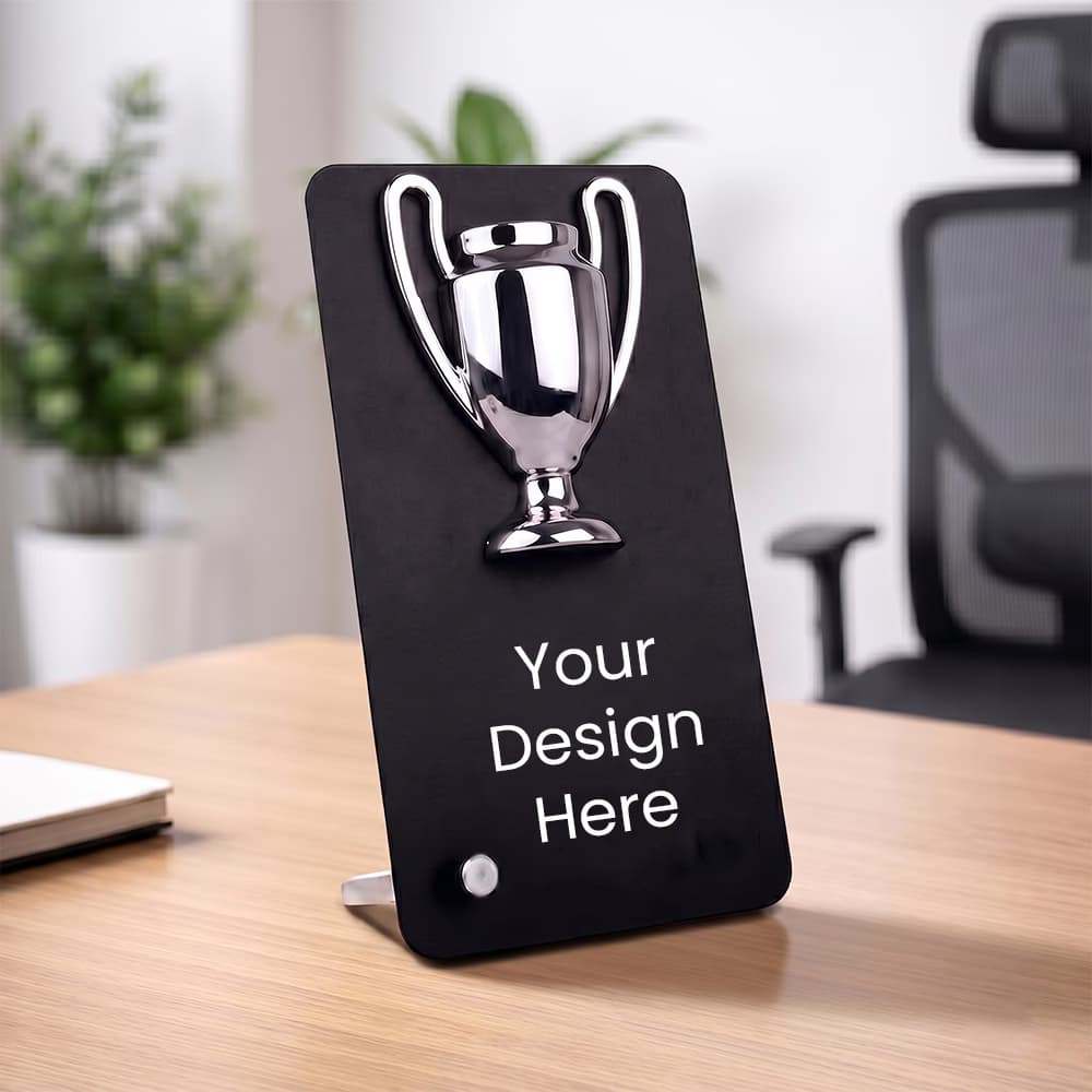 A customizable black Winner Cup Desk Trophy with a chrome cup emblem and "Your Design Here" placeholder text on a wooden office desk.
