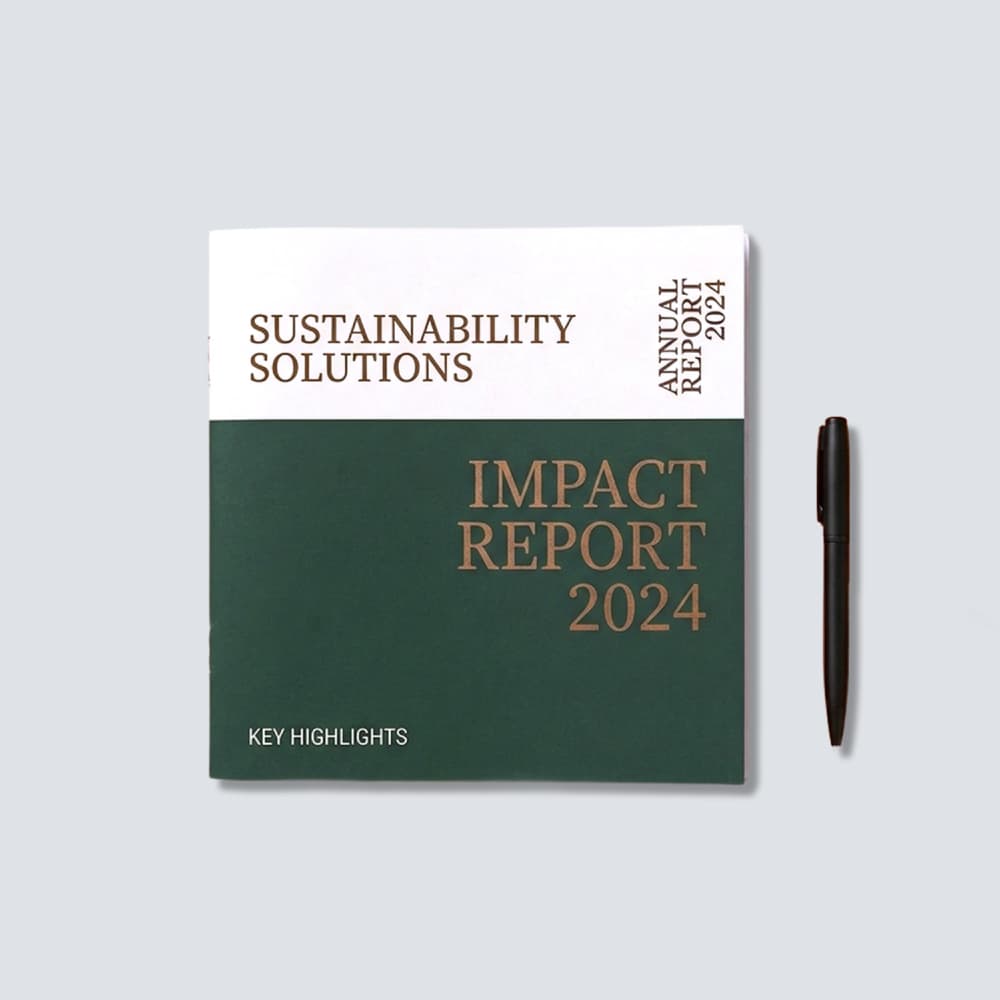 Front cover of a 2024 Sustainability 6x6 booklet in green and white, placed flat on a grey surface next to a sleek black pen.