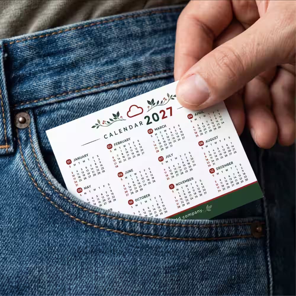 Close-up of a hand sliding a compact 2027 custom pocket calendar into the front pocket of blue jeans.
