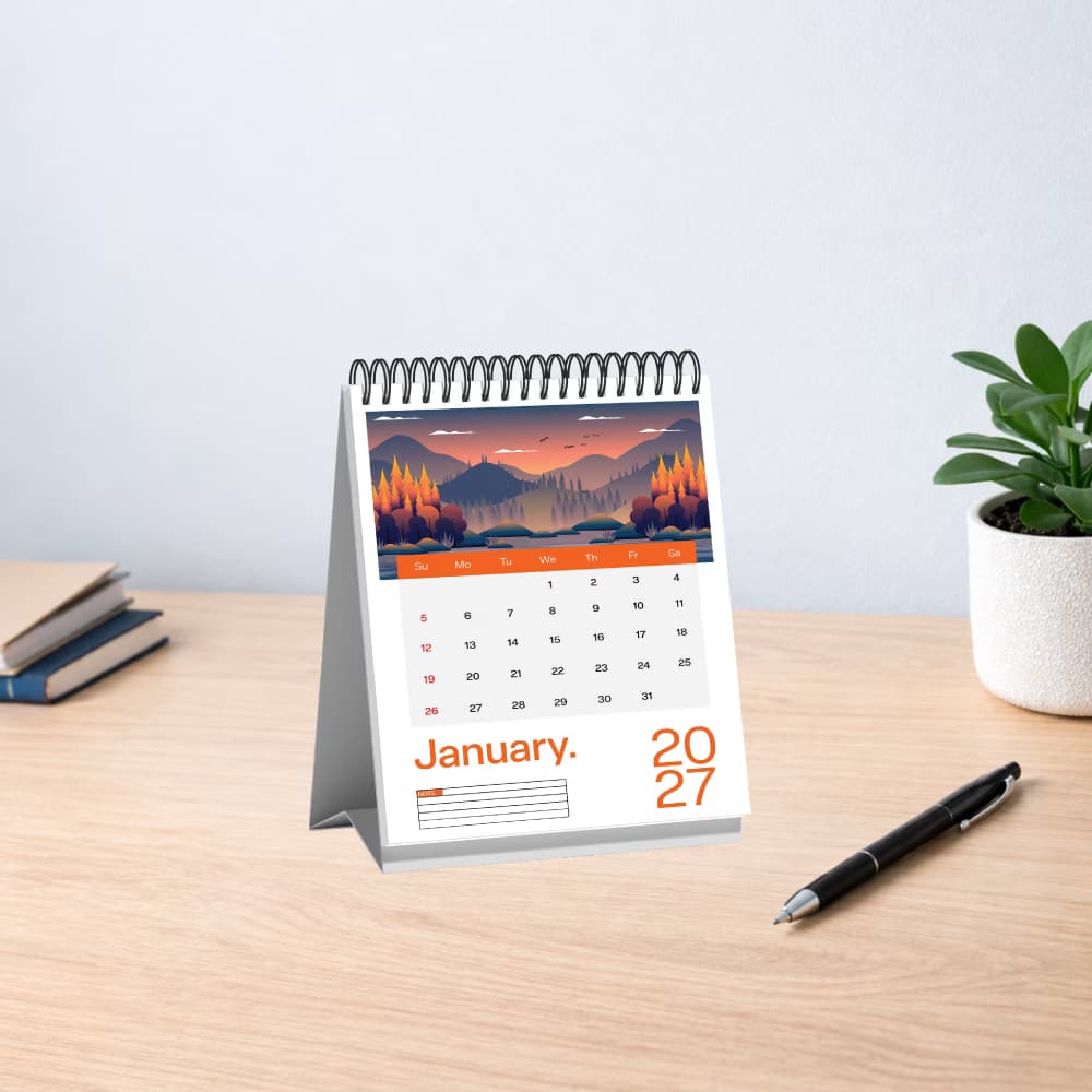 A portrait-oriented 2027 tent-style desk calendar with a nature illustration on a wooden workspace table.