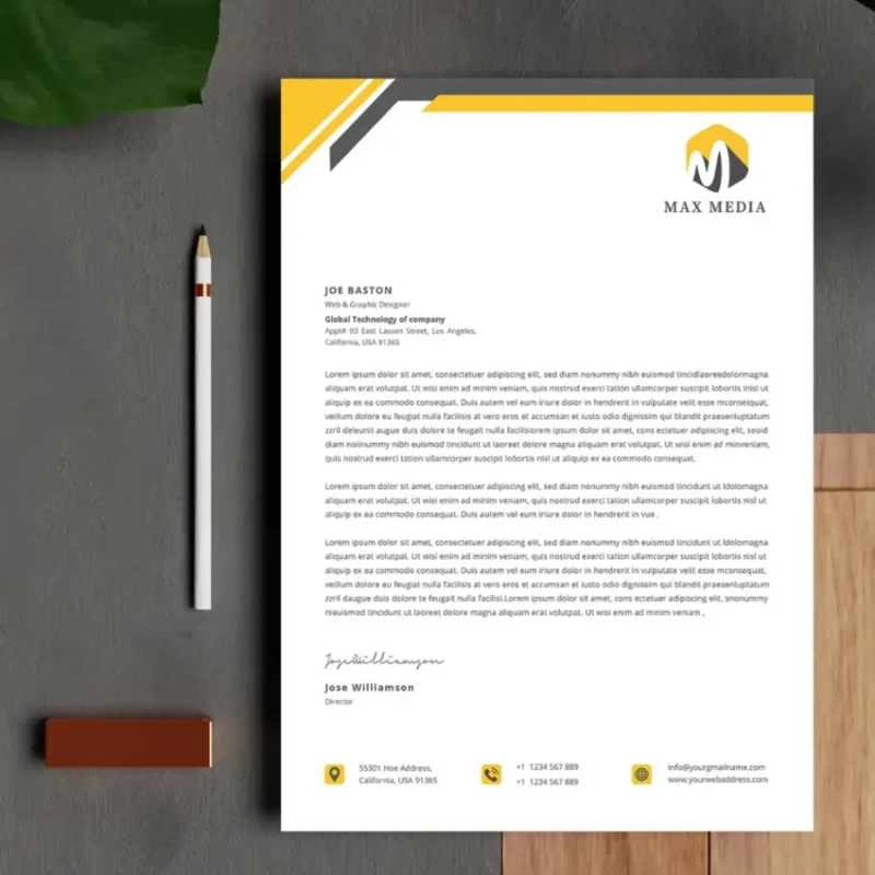 A close-up of a custom letterhead with a yellow and black design on a gray surface, with a pencil and a plant nearby.