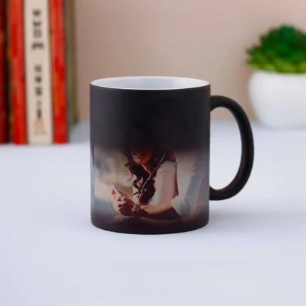 A Quapri Personalized Color-Changing Magic Mug sits on a cozy living room table next to a plate of cookies. The mug displays a vibrant design as it’s filled with steaming tea.