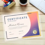 Laminated certificate for Mahesh Kumar with a purple-orange gradient on a wooden desk with coffee.
