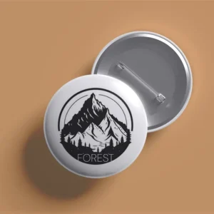 Overlapping front and back views of a white circular pin featuring a black mountain and forest illustration.