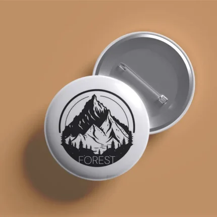 Overlapping front and back views of a white circular pin featuring a black mountain and forest illustration.