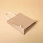 Angled top view of an empty, eco-friendly jute bag with white rope handles resting on a tan surface.