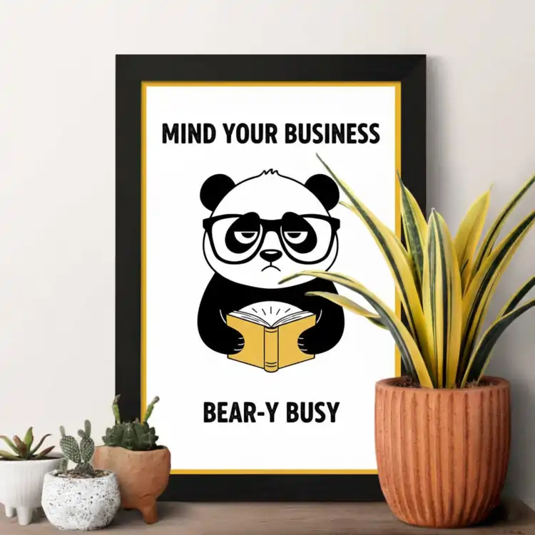 Framed art of a Luxury Photo Frames grumpy panda reading a book with the text "Mind your business, bear-y busy." Small potted plants sit in the foreground