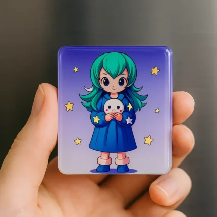 A hand holding a square magnet featuring an anime style girl with green hair holding a plush toy against a starry purple sky