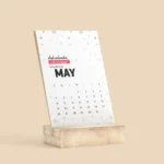 A Desk Calendar With Wooden Stand displaying the month of May. The calendar has a modern, minimal design with geometric patterns and an A5-sized full-colour sheet.