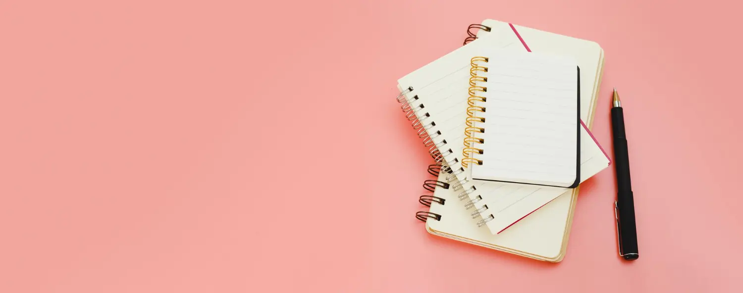 Banner image featuring the text 'The Most Asked Questions About Notebook' on a pink background, with a stack of various-sized spiral notebooks and a black pen on the right side.