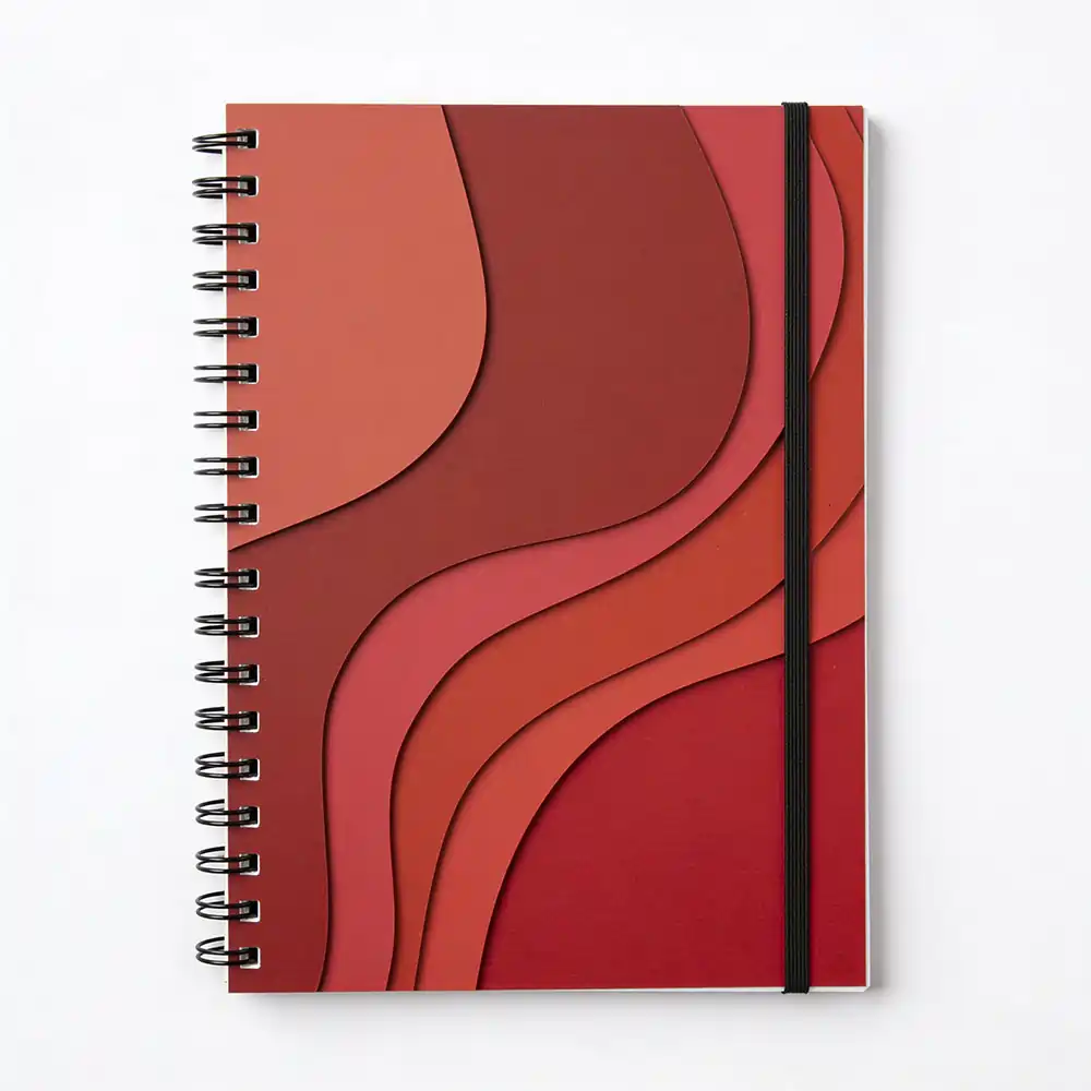Top-down view of a red wiro notebook with wavy, layered paper-cut art on the cover and a black elastic closure band.