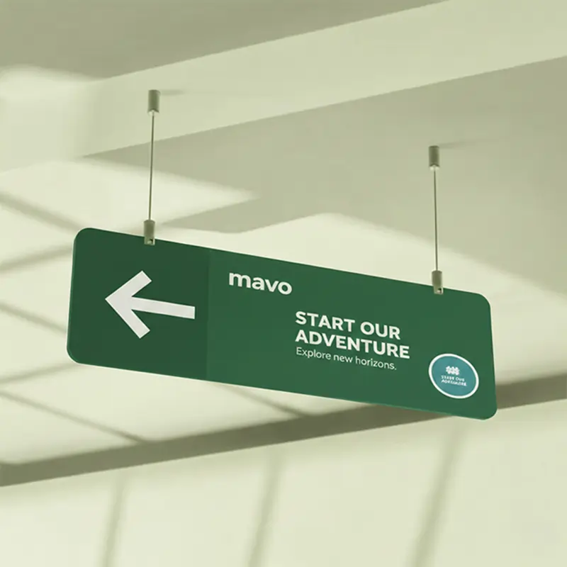 A green hanging directional sign featuring a white arrow, mavo logo, and "Start Our Adventure" slogan.